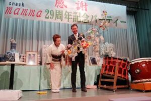 「スナックマンマ」の29周年チャリティパーティーでまゆ玉に下がった善意19万円余りを中心市街地活性化に役立てて五十嵐店主が国定市長に手渡す