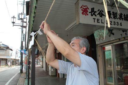 店の前に張られた荒縄にイネと紙垂を下げる長谷源製菓舗の主人