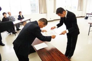 無投票で三条市長選で3選を果たした国定市長(右)に三条市選挙管理委員会の高野委員長から当選証書を手渡す