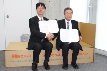 段ボール製の簡易ベッド「暖段はこベッド」に座って協定を結んだ燕市の鈴木市長(左)とセッツカートンの酒井常務