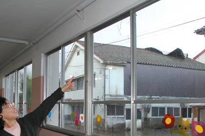 燕東幼稚園の穴の開いたガラス、ガラスの向こうの屋根の上にはがれ落ちたトタンが見える