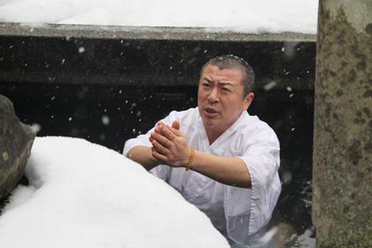 雷井戸の不動明王の野仏に向かって胸まで水柱に沈めて手を合わせる山田住職