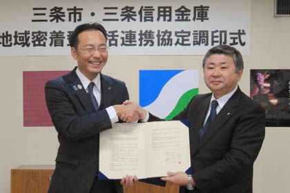 調印した地域密着型包括連携協定の協定書を手に握手する国定市長(左)と三条信用金庫の西潟理事里長