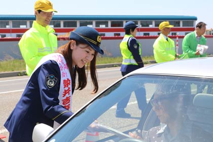  燕市熊森地内で待避所に設置した交通指導所でドライバニーに春の全国交通安全運動の啓発グッズを手渡す分水おいらん道中で染井吉野太夫を務めた本田さん
