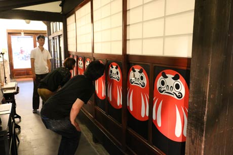 だるまの片目に開けた穴から展示をのぞき見る「のぞきだるま」スタイルで鑑賞