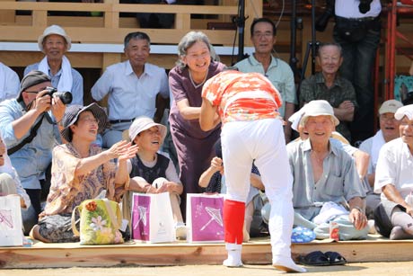 立ち上がってひょっとこの面のウズラと握手するチヨさん