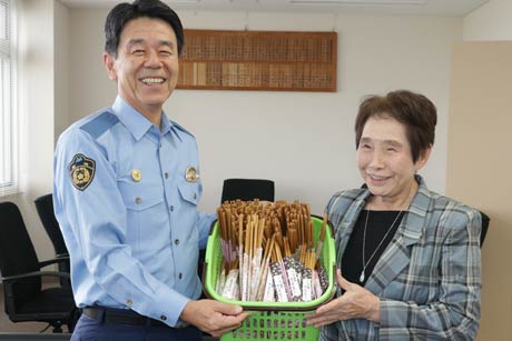 藤さんが手作りした交通安全標語付きのはし袋とタケのはしのセットを手に藤さんと斉藤署長
