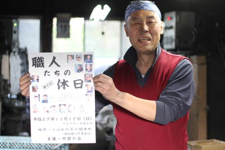 「職人たちの休日」のポスターと会員の川崎栄治さん