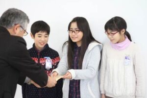 粟生津小の校内募金に寄せられた善意約6千円を燕市社協の島田常務理事に手渡す左から体育ボランティア委員会の副委員長の小平君、委員長の宮路さん、書記の河合さん