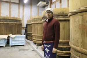 味噌蔵見学と味噌仕込み体験イベントを越後味噌醸造の5トンの木桶の前でイベント担当の木龍さん
