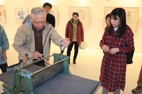 鶴巻貴子銅版画展のワークショップ「エッチングプレス機で版画を作ろう」で会場でエッチングプレス機で版画をする参加者と指導する鶴巻さん(右)