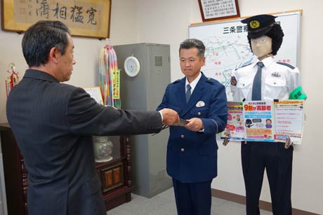 警察官の等身大の人形「のんちゃん」(右)に代わって三条信用金庫の小浦方文之常務理事(左)から感謝状を受け取る大面駐在所勤務の野沢一昭巡査(中)