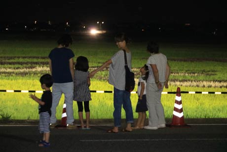 夕涼みがてらに照明に輝く緑のイネを見てはしゃぐ子どもたち