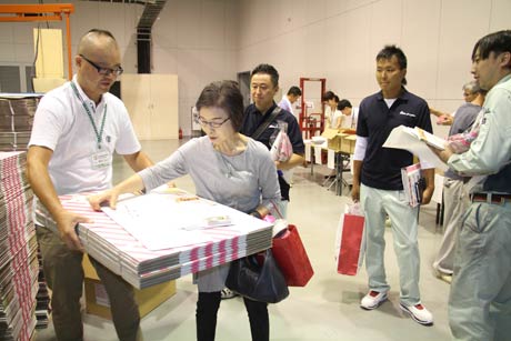 工場の祭典のシンボルといえる斜めのピンクストライプが印刷された段ボール箱など装飾の材料を持ち帰る参加者