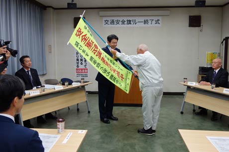  燕市交通安全協会安全運転管理者部会の交通安全旗リレー終了式で交通安全旗を井上砂利店の小黒寛一さんから斎藤燕署長に返還