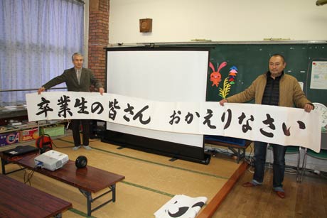 「卒業生の皆さん　おかえりなさい」とある横断幕を掲げて卒業生を迎える
