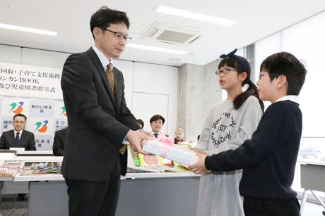 杉名児童管を利用する小池小児童に「カンカンBOOK」事業で購入した児童図書を手渡す和平フレイズMS株式会社の種子管理本部部長から
