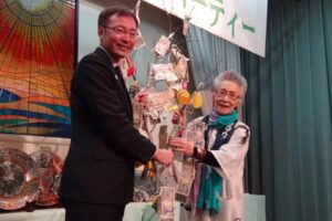 スナックマンマの32周年チャリティパーティーで客がまゆ玉に下げた善意を国定三条市長に手渡す五十嵐さん