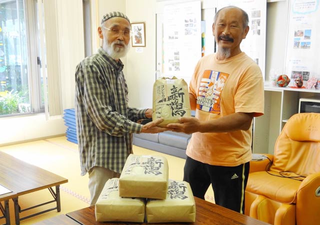 渡辺さん(右)から避難者のための交流ルーム「ひばり」の佐竹代表に新米を手渡す