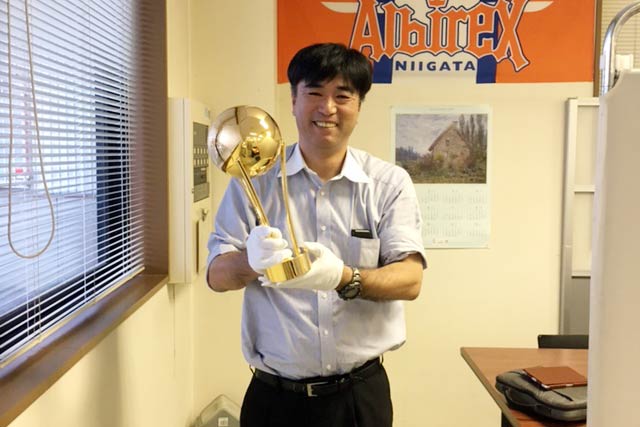 「燕ロータリークラブ杯サッカー大会 U-12」のオリジナル優勝トロフィーを手に台座部分を製作した長谷川挽物製作所の長谷川社長