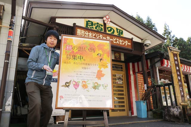燕市分水ビジターサービスセンター前で「国上山　あなたの秋を撮ろうキャンペーン」のポスターと地域おこし協力隊の岡田さん