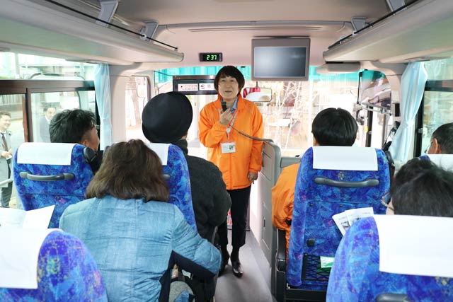 バスの車内で次に向かう工場について話す土橋さん