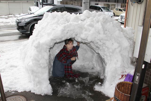 化粧品店「リラ」の前にできた除雪の雪山から作ったかまくらと店主の栄森さん