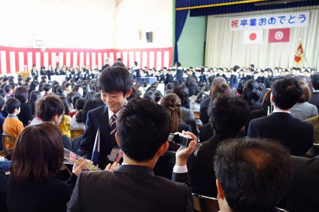 卒業証書を受け取ってガーベラの花束を保護者に手渡す卒業生