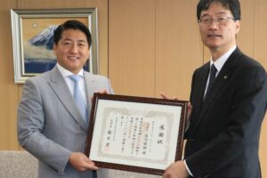 鈴木市長(右)から感謝状を受けるアイム・ユニバースの藍澤代表取締役