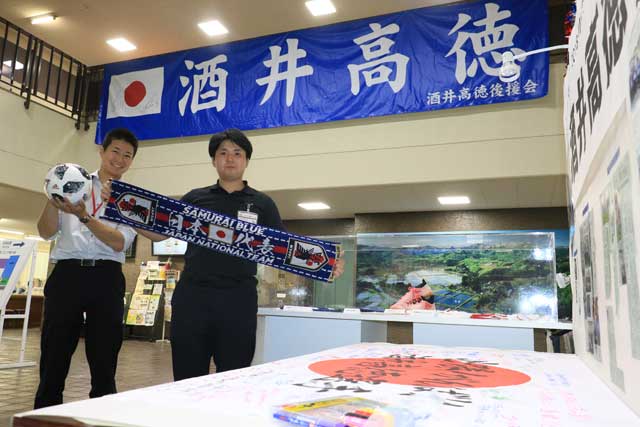 三条市役所正面玄関に日の丸の応援メッセージ、職員が持つのは「かもめ～る」で応援メッセージを出した人に抽選で当たる賞品のW杯公式試合球と日本代表2018オフィシャルタオルマフラー
