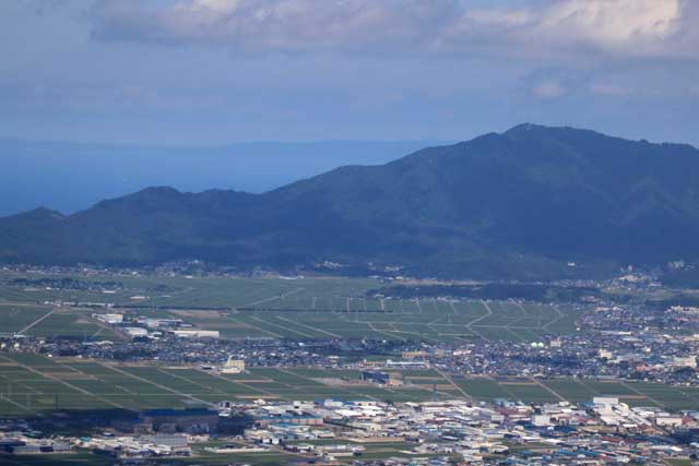 ヘリコプターから弥彦山の肩越しにのびる佐渡の稜線が見える