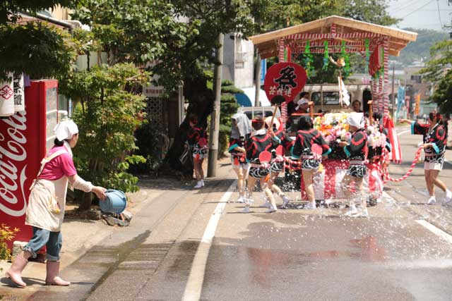 沿道の店舗は涼しくなればと打ち水でサポート