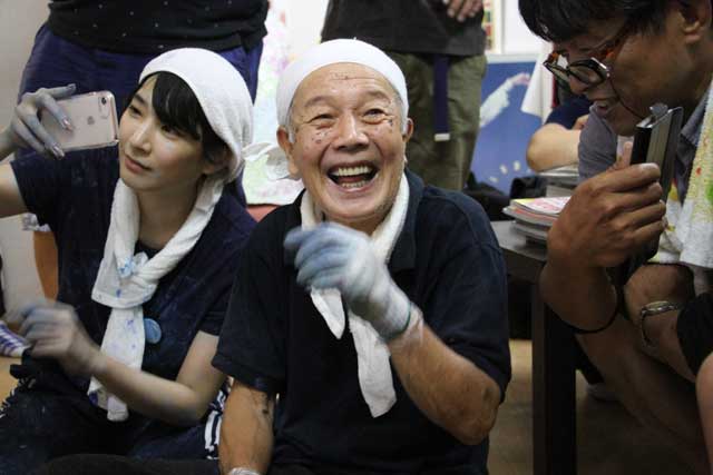 自身のライブペインティングを報道するテレビニュースを喜ぶ丸山さん