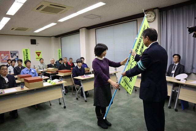 春木建設の副安全運転管理者、山崎美代子さんから渋谷署長に交通安全旗を手渡す