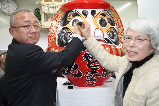 小林氏が妻君子さんと手と手を取ってだるまの目入れ
