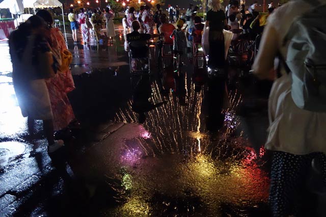 雨にぬれたアスファルトに映る花火
