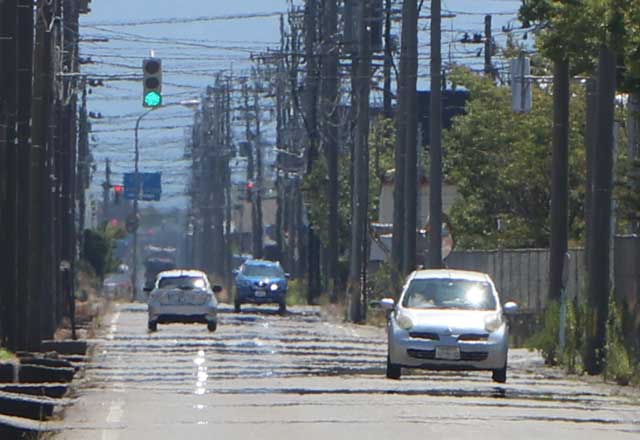 燕市小関地内の道路にあらわれた逃げ水とかげろうで景色が揺れる