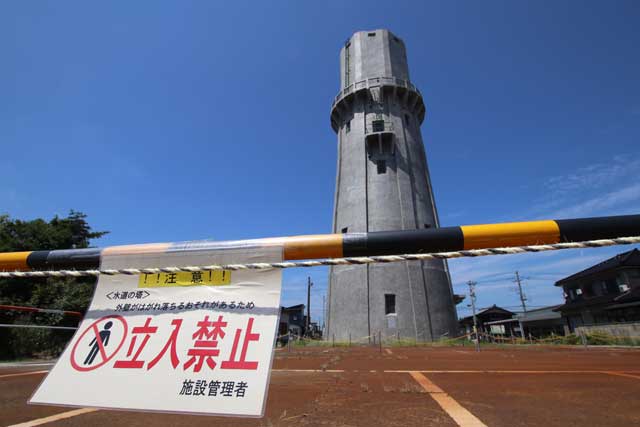 外壁がはがれ落ちて周辺を立ち入り禁止にしている燕市総合文化センター駐車場に立つ旧浄水場配水塔