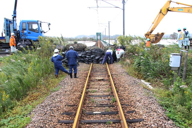 堤防が切り下げられている越後線の線路部分に石や砂を詰めたパックを積む