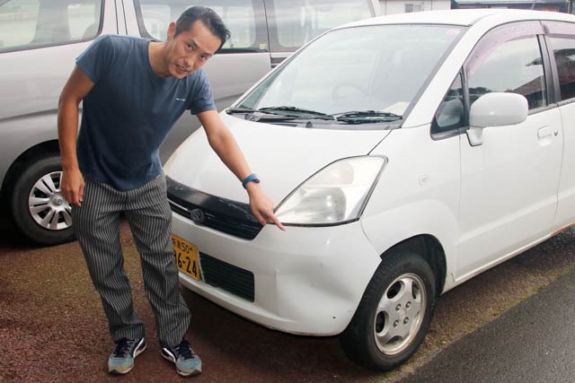 クマとぶつかった軽自動車のへこんだバンパーを指さす地域おこし協力隊の渡辺さん