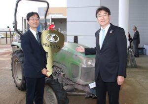 寄贈を受けたトラクターの前で鈴木燕市長(左)とクボタの飯塚執行役員