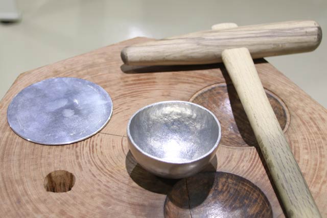 錫ぐい呑み製作体験で作るぐい呑み（中央）と材料の錫の板(左)、製作に使う木づち(右)、ケヤキ材の型(下)