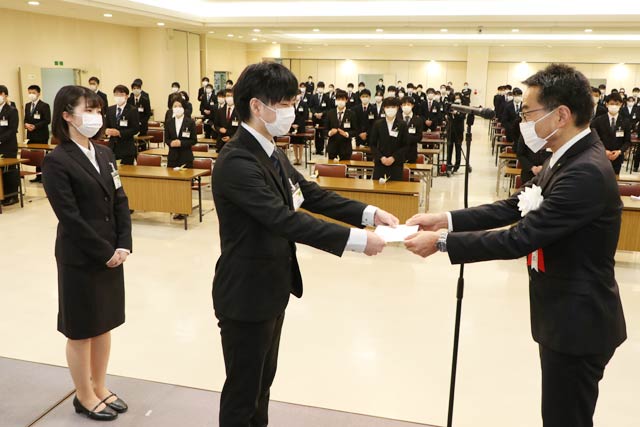 コメリグループ入社式で捧社長から新入社員代表に辞令を手渡す