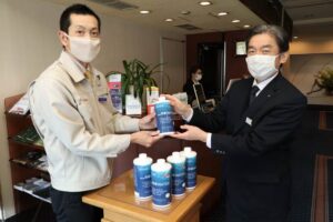 越前屋ホテルの明田川代表社員(右)に除菌液を手渡す梨本商店の梨本社長