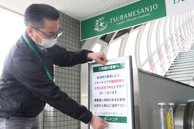 燕三条地場産業振興センター・リサーチコア入り口に利用中止を知らせる案内を張る職員
