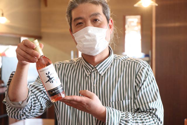加茂市の飲食店応援キャンペーンに岩の原葡萄園が提供したワイン「善 ロゼ 360ml」を手に5,000円以上の注文でこのワインをプレゼントする「サントピアット」の桑原店主
