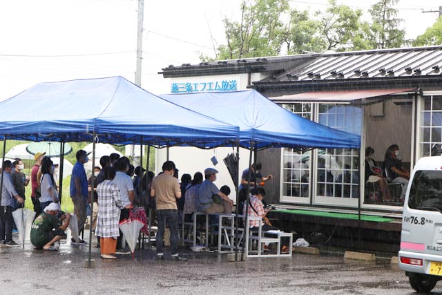 雨のなかテントの下でスタジオを見学のファン