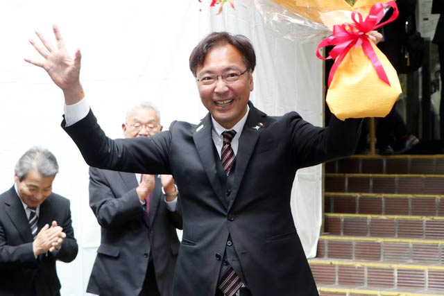 市役所正面玄関前で見送りに集まった職員に手を振って退庁する国定市長