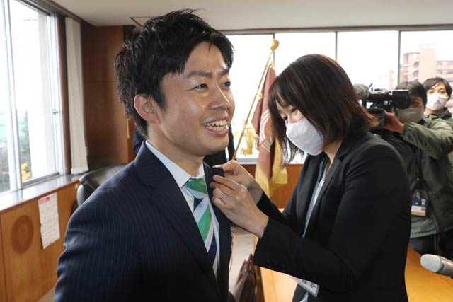 市長室で職員から市長記章や名札を付けてもらう
