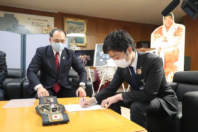 名誉会長の就任承諾署名証書に署名する滝沢市長